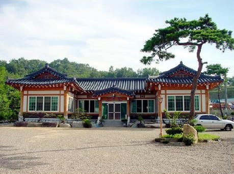 큰 소나무와 자갈 마당 너머의 기와집 외관